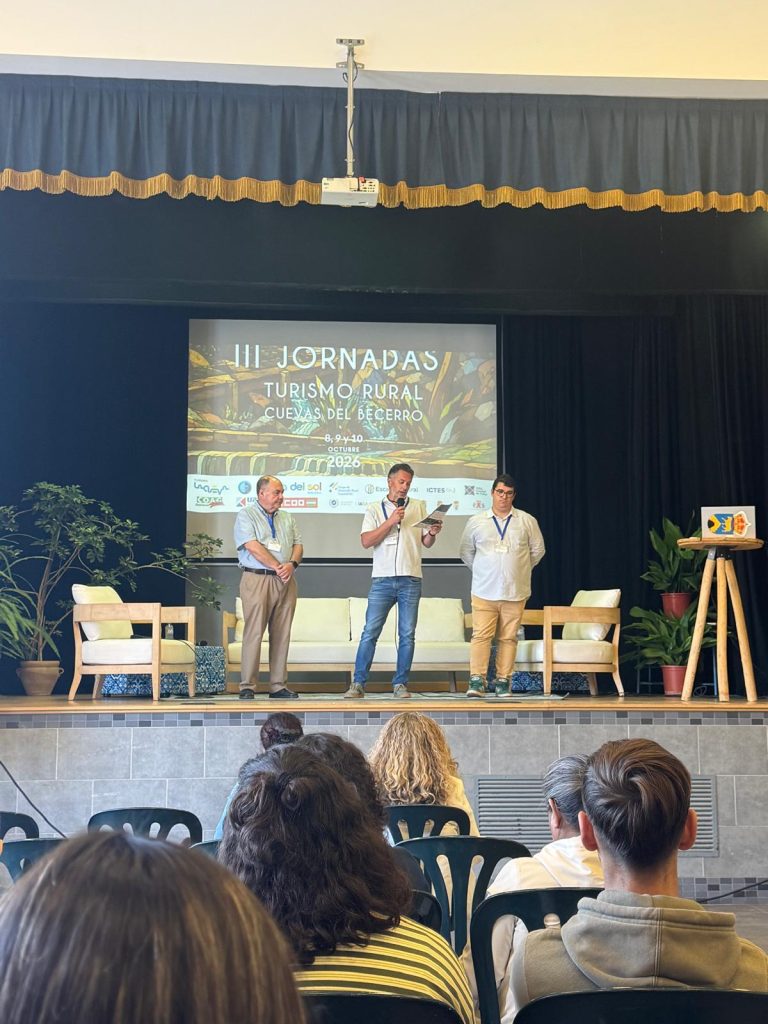 Tres participantes en el escenario de las III Jornadas de Turismo Rural de Cuevas del Becerro, uno de ellos interviniendo ante el público.